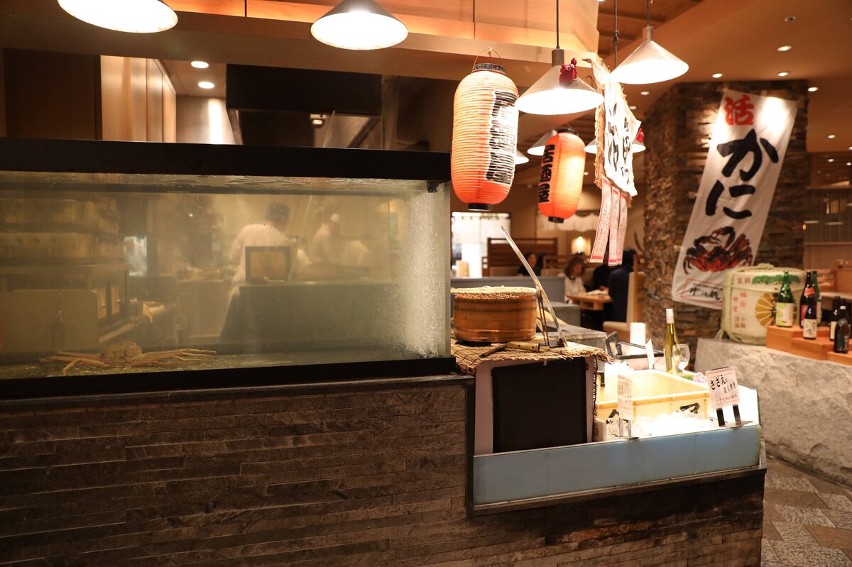 水槽に入ったカニや調理場の様子、提灯などがある飲食店内の写真