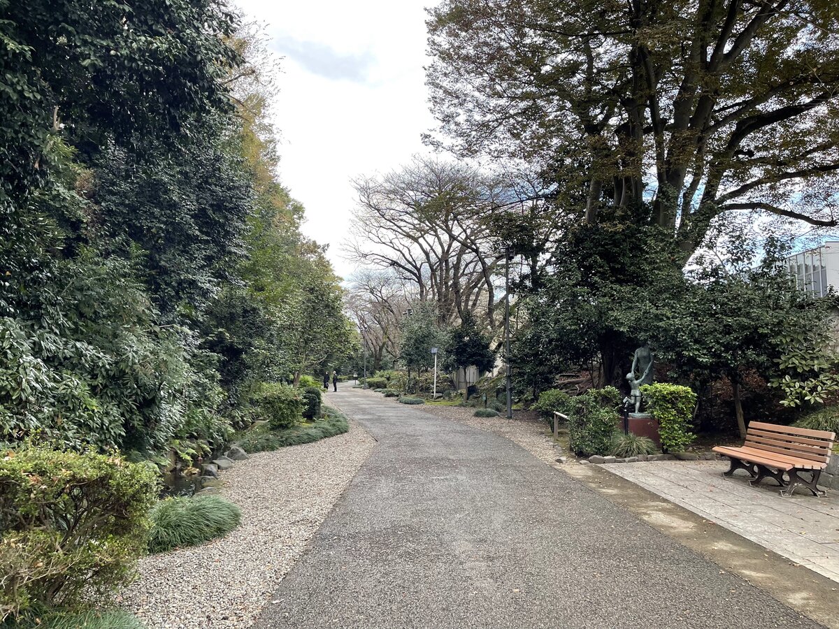 庭園の風景。松の木、石垣、銅像が見える。