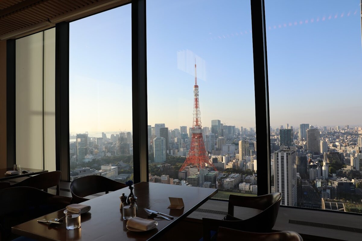東京エディション虎ノ門：テーブルにティーセットと軽食、窓の外には東京タワーが見え...