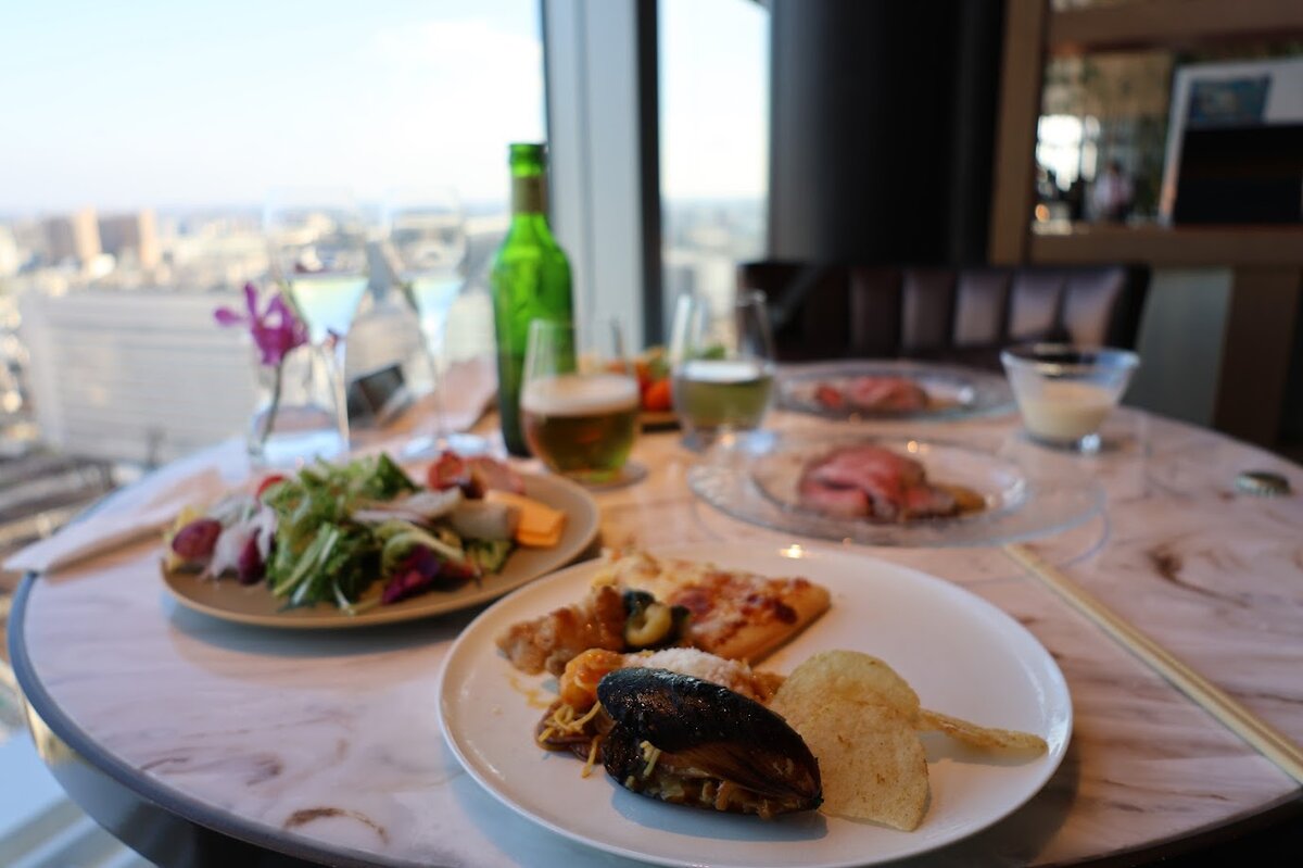 名古屋マリオットアソシアホテル：高層階からの景色を背景にしたテーブル上の料理