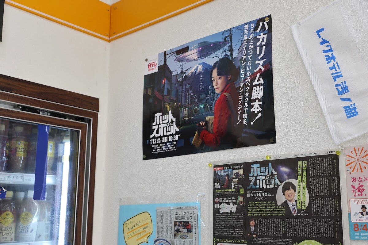 コンビニ店内：施設内の壁に、番組ポスターやグッズなどが貼られている。記...